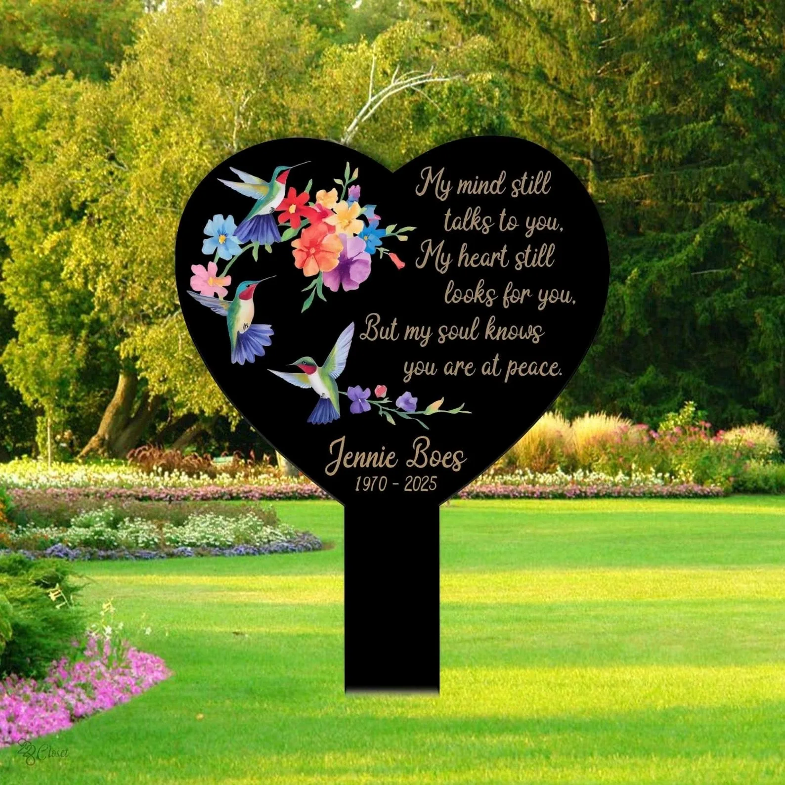 style-25.-Heart-Hummingbirds-3 Black heart-shaped memorial plaque in a sunny garden with hummingbirds, flowers and text reading a condolence poem and name Jennie Boes 1970–2025