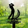 Black metal memorial yard stake showing a golfer silhouette, decorative crescent shape, text "DAD" and dates "1962 - 2023" placed in a grassy outdoor setting