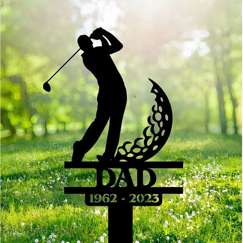 Black metal memorial yard stake showing a golfer silhouette, decorative crescent shape, text "DAD" and dates "1962 - 2023" placed in a grassy outdoor setting