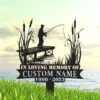 Silhouette memorial sign of a fisherman on a dock with cattails over water, text reading "In Loving Memory of" and placeholder "Custom Name 1960-2023" in grassy foreground