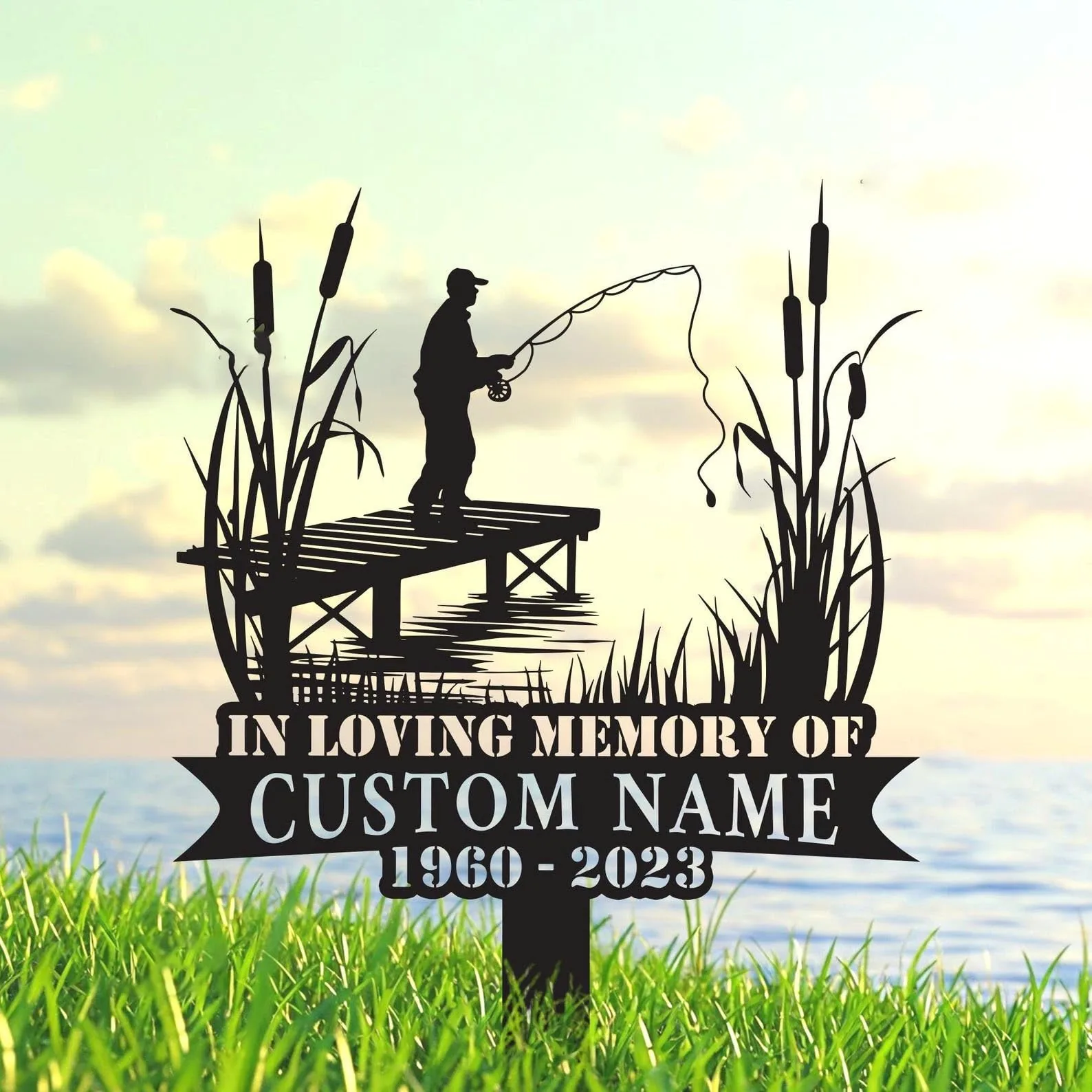 Silhouette memorial sign of a fisherman on a dock with cattails over water, text reading "In Loving Memory of" and placeholder "Custom Name 1960-2023" in grassy foreground