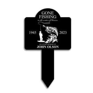 Black memorial garden stake reading "Gone Fishing" with fish illustration, years 1945–2023 and "In loving memory of John Olson"