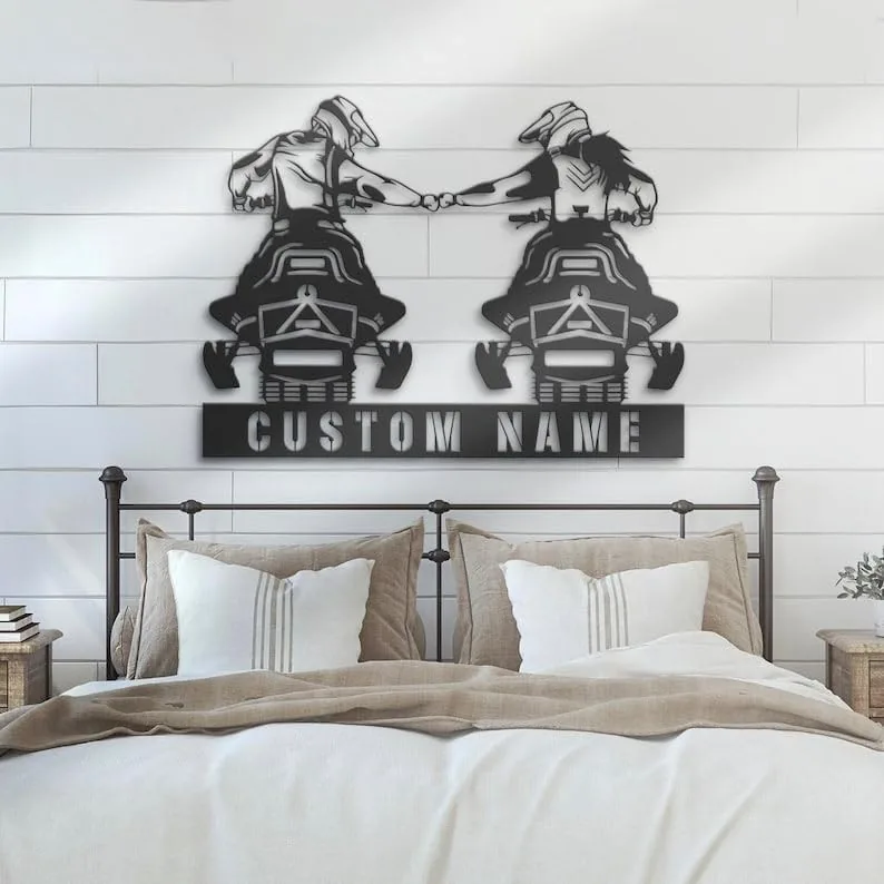 Metal wall art of two people riding ATVs fist-bumping above a customizable "CUSTOM NAME" sign, mounted above a farmhouse-style bed in a neutral bedroom