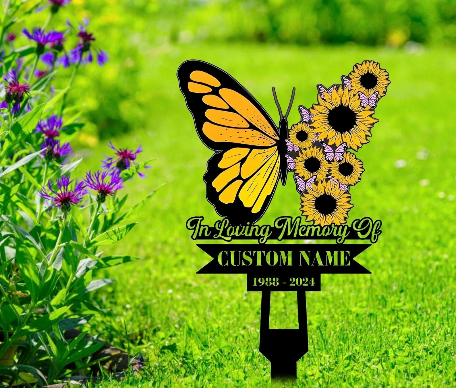 Memorial garden stake with a large yellow and black butterfly wing and sunflower cluster, text reading "In Loving Memory Of" and placeholder "CUSTOM NAME" with dates, placed in a green lawn near purple flowers