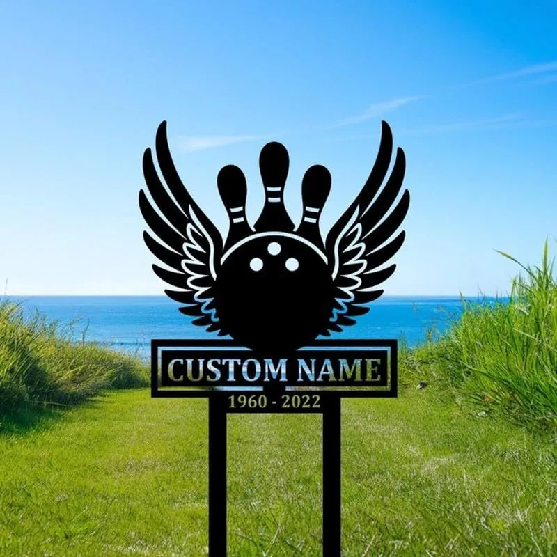 Black metal yard sign of a winged bowling ball and pins with text 'CUSTOM NAME' and dates '1960 - 2022' placed on grassy coastal lawn by the ocean