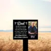 Black memorial sign in a wheat field reading “Dad” with poem lines, photo of an older smiling man and text “In loving memory Robert 1945–2022”