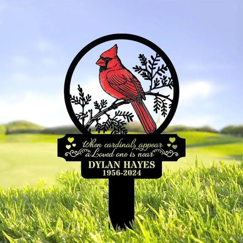 Memorial yard stake with a red cardinal illustration and text "When cardinals appear a Loved one is near" and name "Dylan Hayes 1956-2024" placed in grass