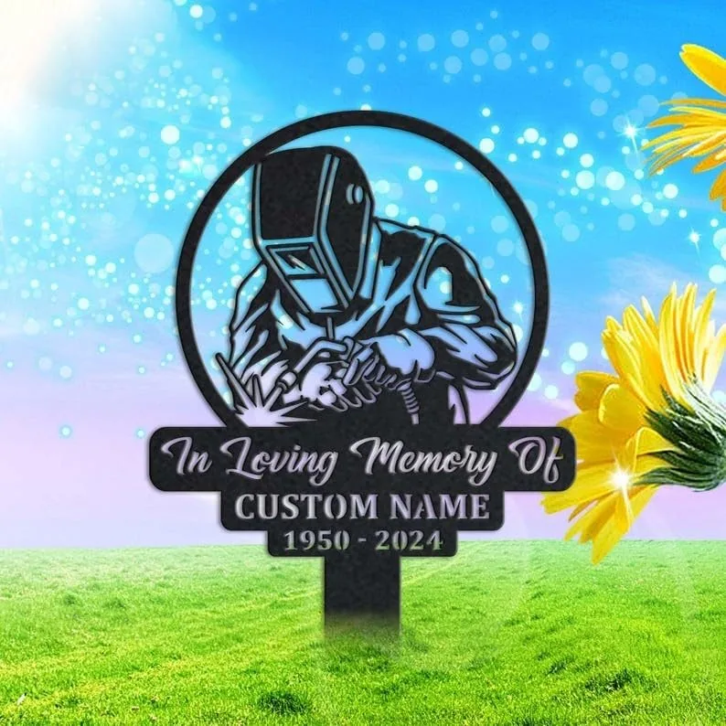 style-36.-Welder-Memorial-3 Grave marker sign with a welder in a helmet, text reading “In Loving Memory Of” and customizable name and years 1950–2024, shown on grass with sunny sky and flowers
