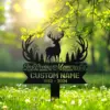 Black metal memorial lawn sign with deer silhouette, trees and antler wreath reading "In Loving Memory" and placeholder text "CUSTOM NAME 1982 - 2024" in a sunny grassy garden