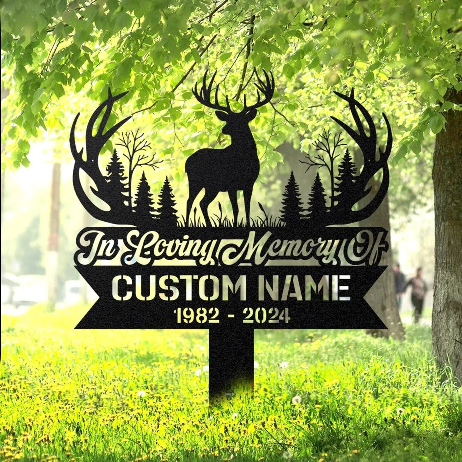 Black metal memorial yard sign with a deer silhouette, trees and antler design reading "In Loving Memory" and placeholder "Custom Name" with dates 1982 - 2024, staked in a grassy park
