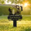 Black memorial yard sign in grass reading "In Loving Memory of Jacob Henderson 1956 - 2024" with silhouette of fisherman reeling a large fish at sunrise