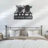 Black metal wall art of two sheep peeking over a sign reading "CUSTOM NAME" hung above a farmhouse bed with neutral pillows and shiplap wall