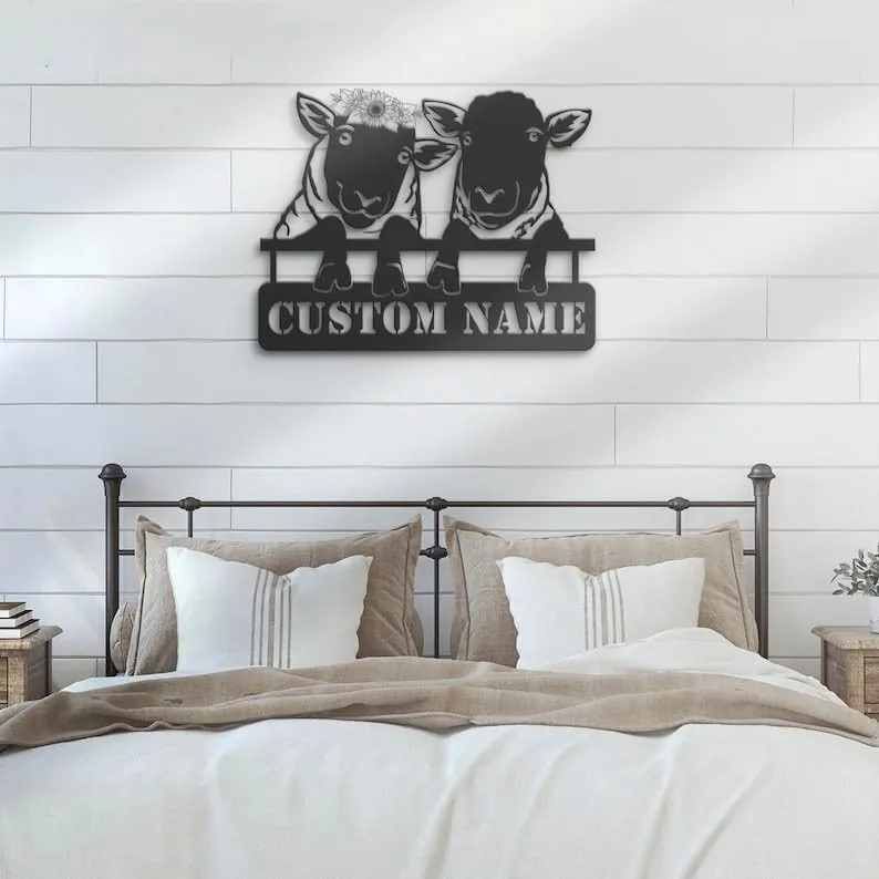 Black metal wall art of two sheep peeking over a sign reading "CUSTOM NAME" hung above a farmhouse bed with neutral pillows and shiplap wall