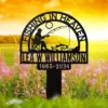 Black metal memorial sign reading "Fishing in Heaven" with silhouette of a seated fisherman and a fish, personalized name and years, shown in a flower field at sunrise