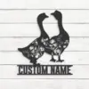 Black metal wall art of two geese with floral cutouts above a customizable "CUSTOM NAME" plaque mounted on white shiplap