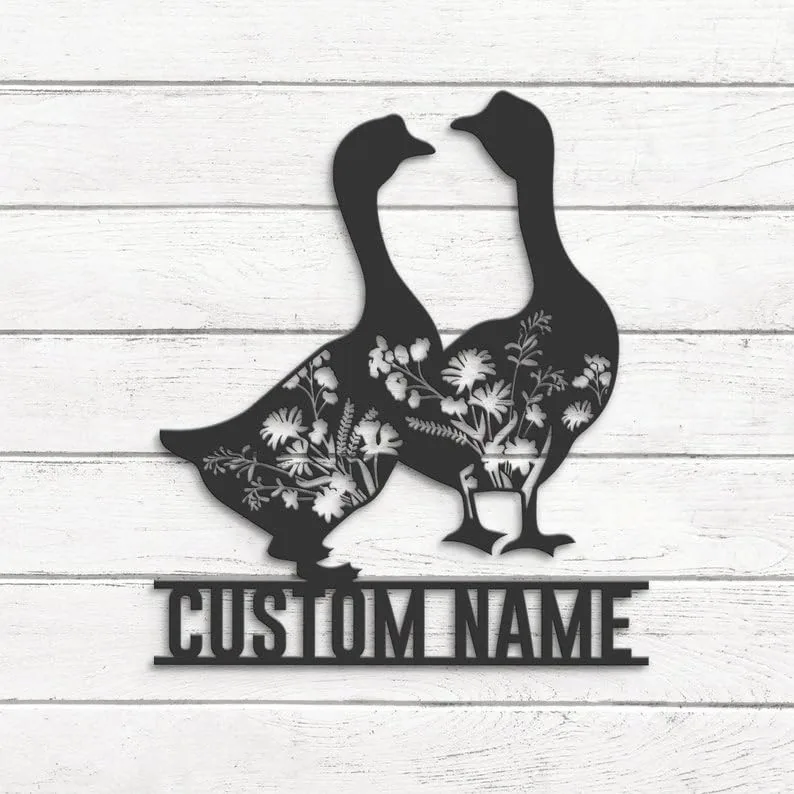 Black metal wall art of two geese with floral cutouts above a customizable "CUSTOM NAME" plaque mounted on white shiplap