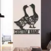 Black metal wall art of two geese with floral cutouts mounted above a customizable name plate in a modern living room