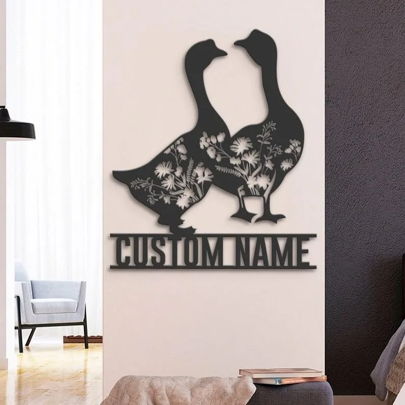 Black metal wall art of two geese with floral cutouts mounted above a customizable name plate in a modern living room