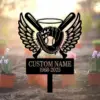 Black metal memorial sign with baseball glove holding a ball, crossed bats and wings above a customizable name and dates, pictured outdoors among potted flowers