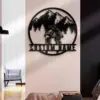 Black metal wall art of two cyclists riding toward mountains and pine trees with placeholder text “CUSTOM NAME,” mounted on a living room wall