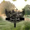 Black metal memorial lawn sign with winged tractor illustration and text "Russel Smith 1963-2025" set in a misty park field at sunrise
