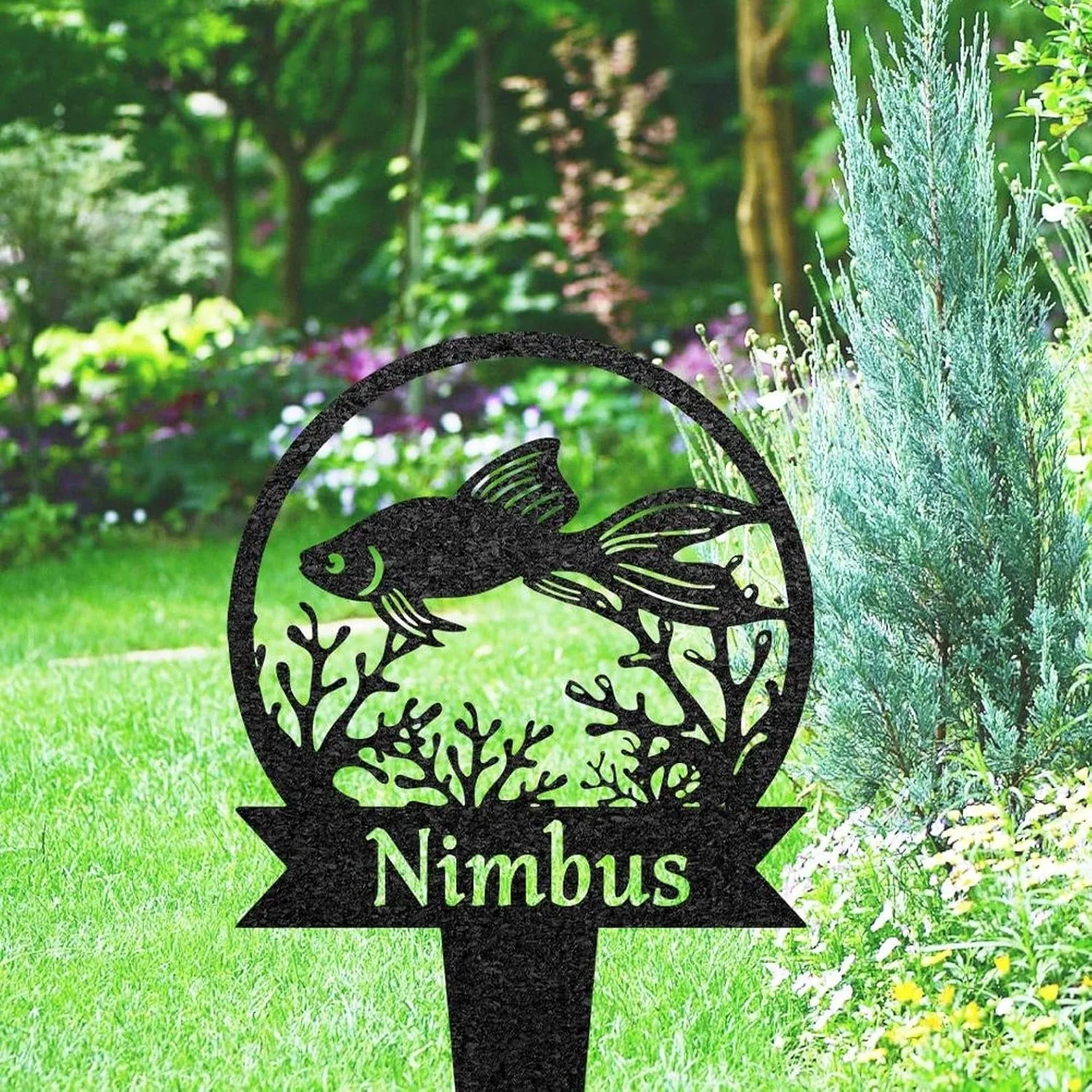 Black metal garden stake with a circular fish and coral cutout and the name "Nimbus" placed in a green lawn beside shrubs and flowering plants