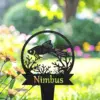 Black metal garden stake with a fish and coral cutout and the name "Nimbus" in front of a blurred sunny garden with orange flowers