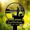 111 Black metal memorial sign showing a fisherman in a boat with a fish, text reading "In Loving Memory of Jacob Henderson 1956 - 2025" against a sunlit grassy background