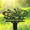 Black metal garden stake shaped like a decorative lizard with leaf and flower cutouts, planted in green grass with sunlight background, text "2021 - 2024" visible