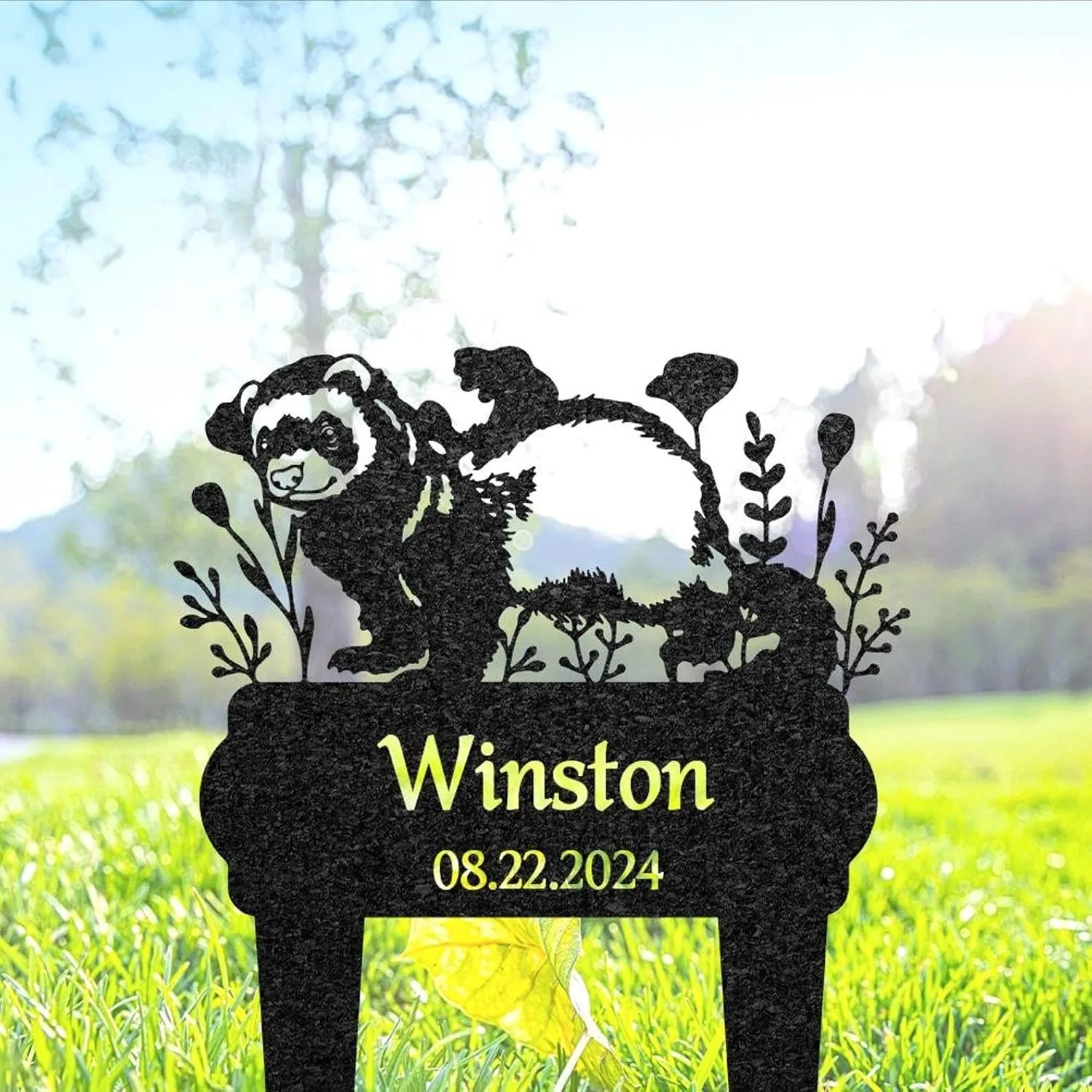 Black garden stake silhouette of a bear with plants and the name "Winston" and date "08.22.2024" staked in grass with blurred trees in background