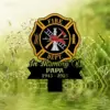 Black and gold Fire Dept. memorial stake with firefighter helmet, ladder, axe and text "In Memory Of PAPA 1945 - 2025" set against dewy green grass background