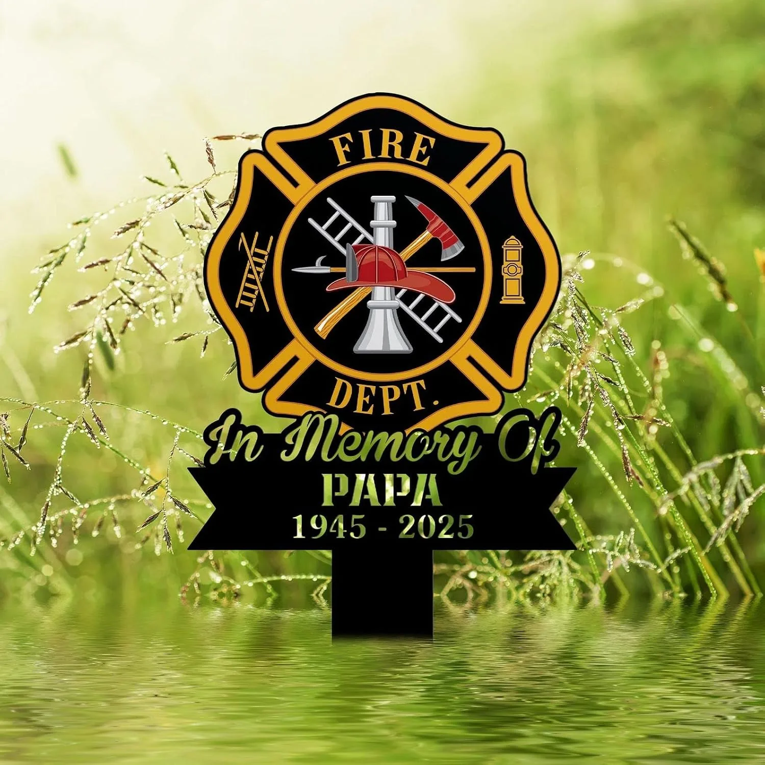 Black and gold Fire Dept. memorial stake with firefighter helmet, ladder, axe and text "In Memory Of PAPA 1945 - 2025" set against dewy green grass background