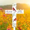 White memorial cross in a sunlit wildflower field reading "In loving memory of Emily 1963-2024" with red cardinals and floral accents