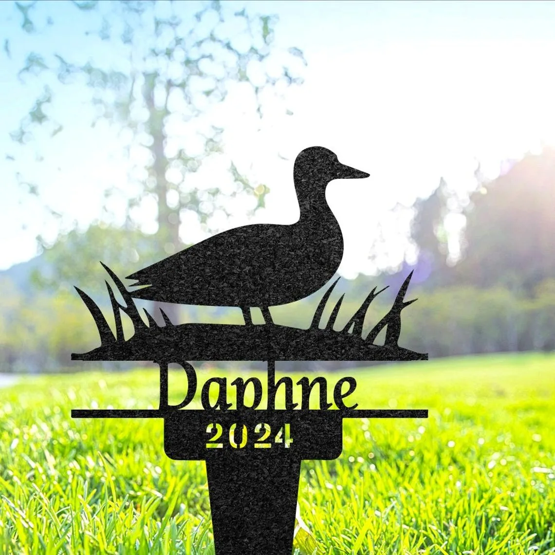 Black metal yard stake with a duck silhouette, grass details and the name "Daphne" with "2024" placed in a sunny lawn setting