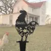 Black rooster yard stake with floral cutouts and the name “Skittles” in front of a farmhouse lawn and a roaming chicken