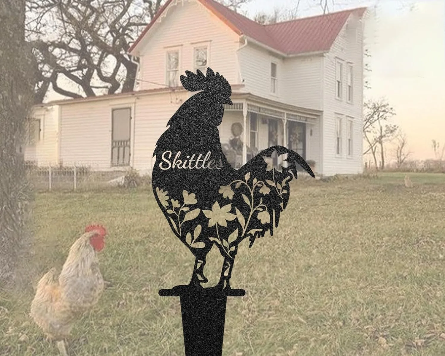 Black rooster yard stake with floral cutouts and the name “Skittles” in front of a farmhouse lawn and a roaming chicken