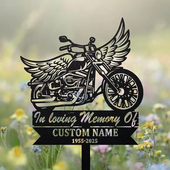 Black metal memorial stake in a flower field depicting a winged motorcycle and text reading "In loving Memory Of" with placeholder "CUSTOM NAME" and years "1955-2025"