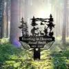 Black metal memorial sign reading "Hunting in Heaven" and "Russel Smith 1963 - 2025" with hunter silhouette, deer, trees and angel wings set in a sunlit forest