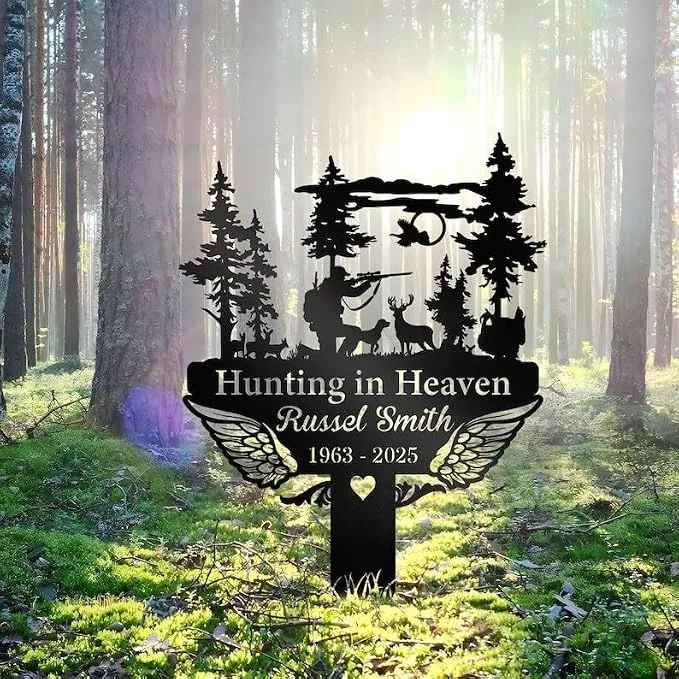 Black metal memorial sign reading "Hunting in Heaven" and "Russel Smith 1963 - 2025" with hunter silhouette, deer, trees and angel wings set in a sunlit forest