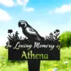 Black garden memorial stake with parrot silhouette and flowers reading "In Loving Memory of Athena" placed in green grass under blue sky
