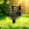 Black metal memorial sign reading "Hunting in Heaven" with name "Russel Smith" and dates "1963 - 2025," silhouette of a hunter, deer, trees and angel wings staked in sunlit grass