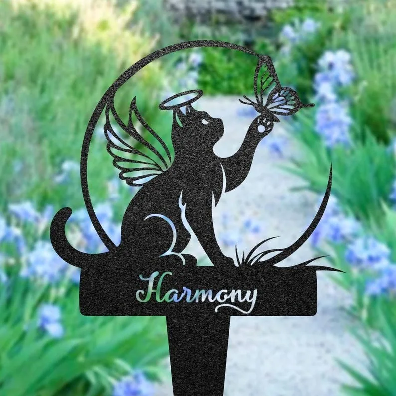 Black garden stake silhouette of a winged cat with halo reaching for a butterfly, word "Harmony" on the base against a blurred flowered garden path
