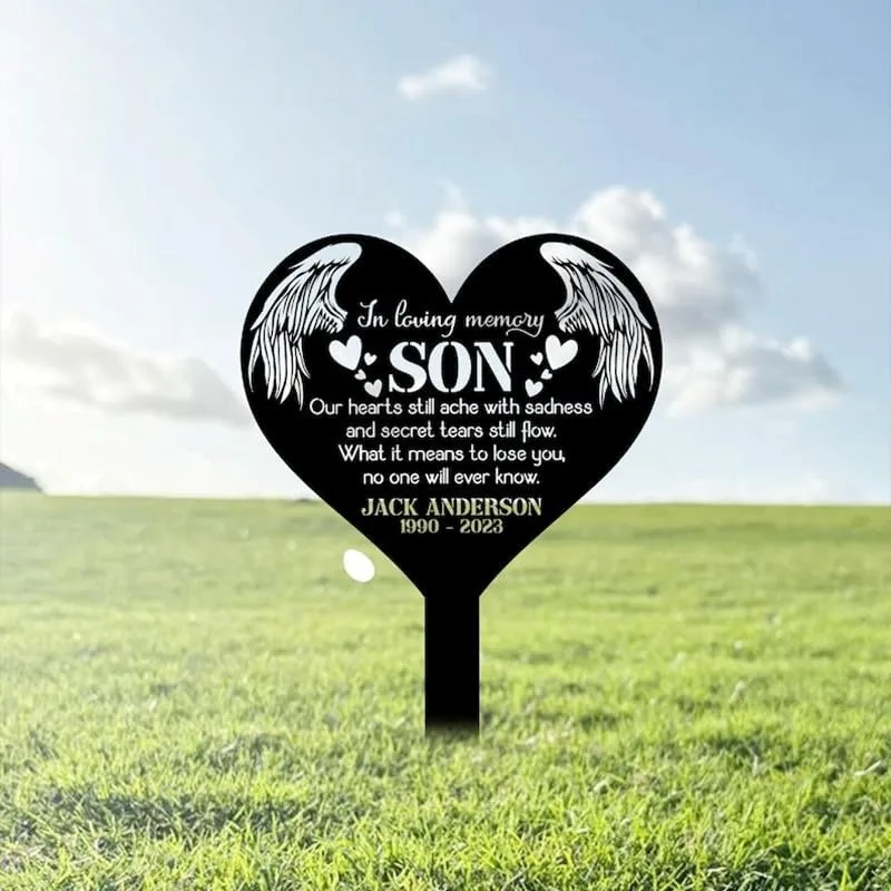 Black heart-shaped memorial stake in a grassy field reading "In loving memory SON" with angel wings, poem lines and name "Jack Anderson 1990 - 2023"