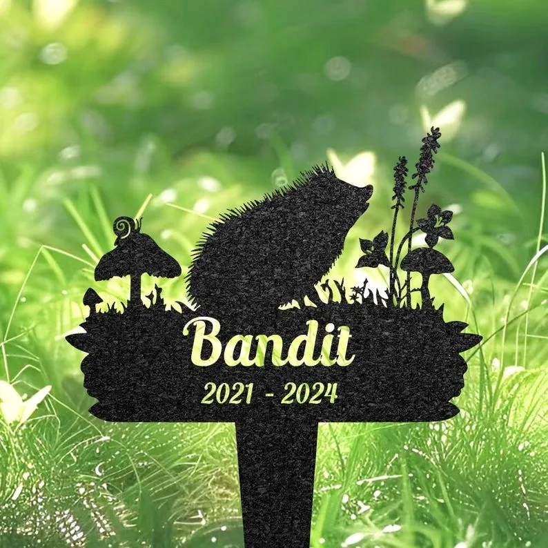 Black garden memorial stake shaped like a hedgehog with mushrooms and plants, text "Bandit 2021 - 2024" on a grassy background
