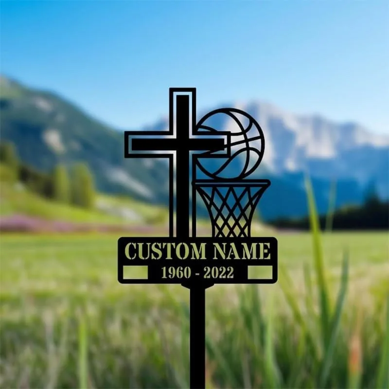 Black metal yard memorial stake shaped like a cross and basketball hoop with a basketball, reading "CUSTOM NAME" and dates "1960 - 2022" against a blurred grassy mountain landscape