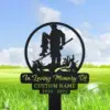 Black metal memorial garden stake showing a fisherman holding a fish inside a circle, with text reading 'In Loving Memory Of', 'CUSTOM NAME' and years '1950 - 2023', placed in grassy outdoor setting