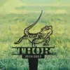 Black metal yard sign of a bearded dragon lizard above the name THOR and dates 2019-2024 placed in a grassy lawn