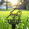 Black metal garden stake shaped like a lizard with the name THOR and dates 2019-2024 set in sunlit dewy grass