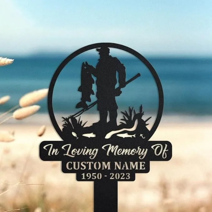 Black metal memorial stake showing a fisherman holding a fish with 'In Loving Memory Of' and 'CUSTOM NAME 1950-2023', displayed against a beach background