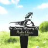 Black grave marker stake with a lizard silhouette and text reading "In Loving Memory Of Parker Chavis 1971-2024" placed in grassy outdoor setting under blue sky